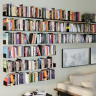 A large wall installation of black shelves filled with books, transforming the room into a spacious, organized home library that enhances the room's décor.