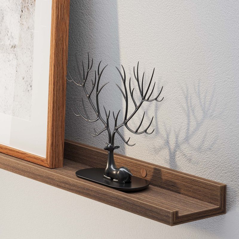 A long floating shelf walnut displays a jewelry holder shaped like a tree with branches, with a framed picture beside it, casting a shadow on the wall.