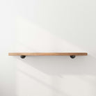 A minimalist floating shelf mounted on a white wall. Supported by industrial-style pipe brackets, the wooden board has a sleek, natural finish, perfect for displaying decor or books.