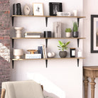 Three floating shelves stacked vertically, styled with neutral décor, books, vases, and plants, blending rustic and contemporary elements.
