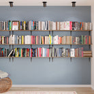 Multi-tiered wall-mounted bookshelves filled with a colorful and extensive book collection, creating a home library feel against a soft blue accent wall.