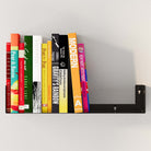 A black metal U-shape book shelf for wall holding several colorful books. The floating book shelf’s sturdy construction supports the weight of multiple books, making it ideal for organizing your reading materials in style.