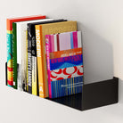 A side view of a black metal U-shape mount book shelf filled with books. The clean lines and contemporary design of the black shelf make it a perfect addition to any modern home decor or office space.