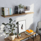 Floating wall shelf is decorated with colorful books, black glass vases, and greenery. Styled above a rustic bench and surrounded by plants, it creates a fresh and organic look for a serene corner.