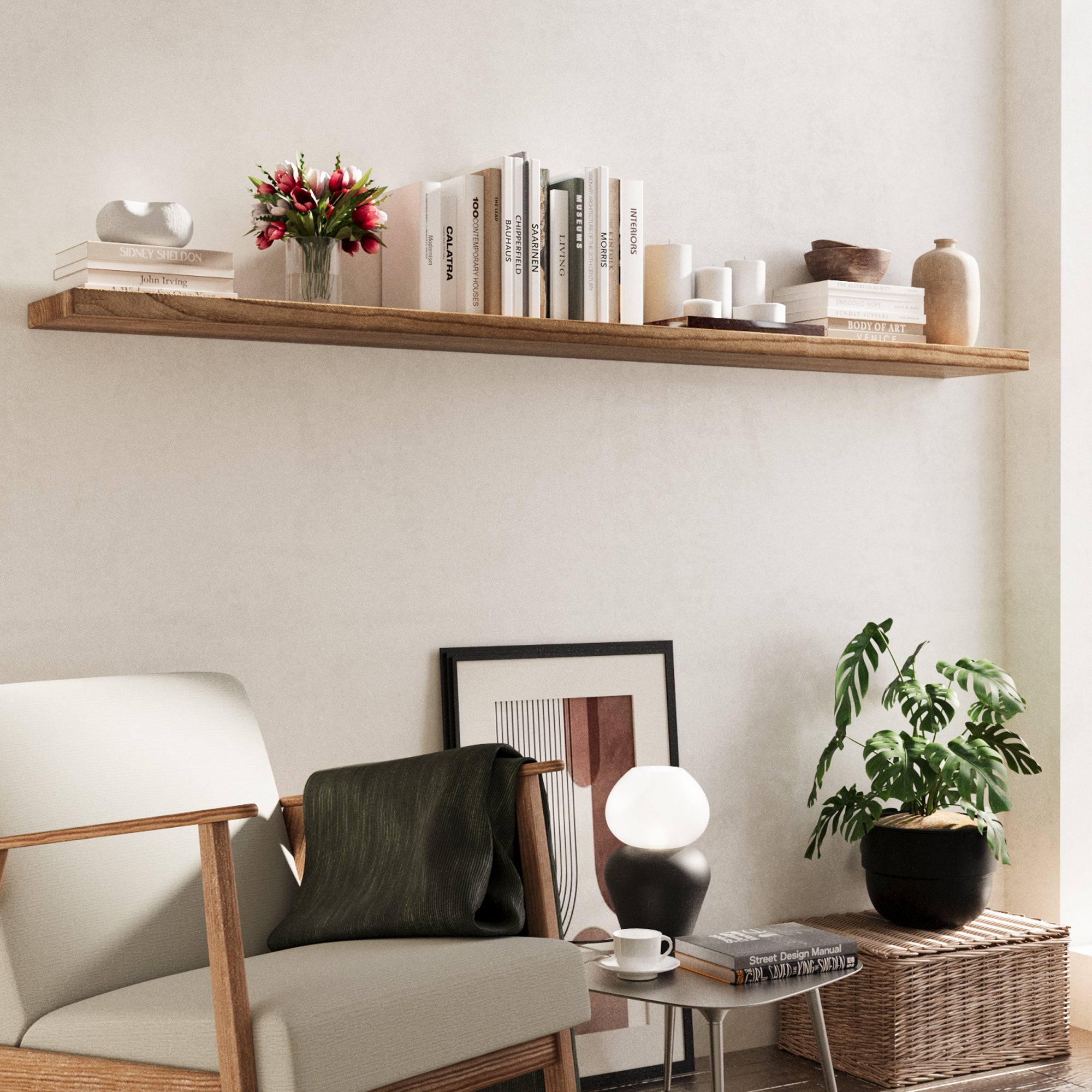 A long wooden shelf above a beige lounge chair, decorated with neutral-toned books, tulips, candles, and sculptural pieces for a soft, cozy reading nook.