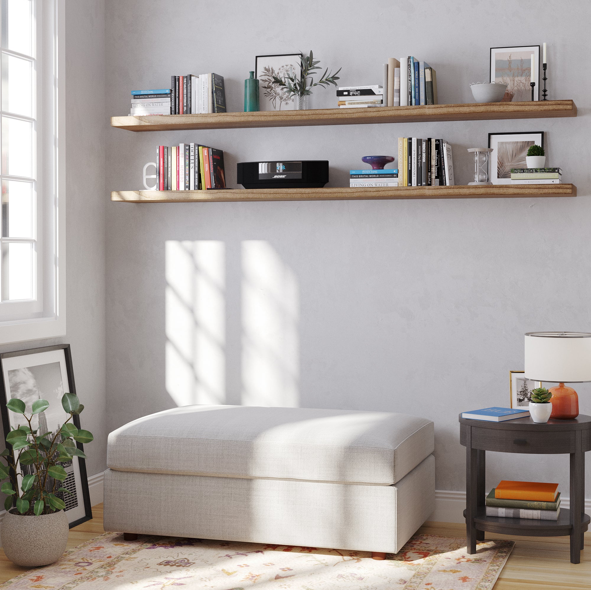 Two wood floating shelves with hidden bracket hold books, vases, and framed art. Sunlight pours in beside a cozy armchair and side table, creating a bright, relaxing corner.