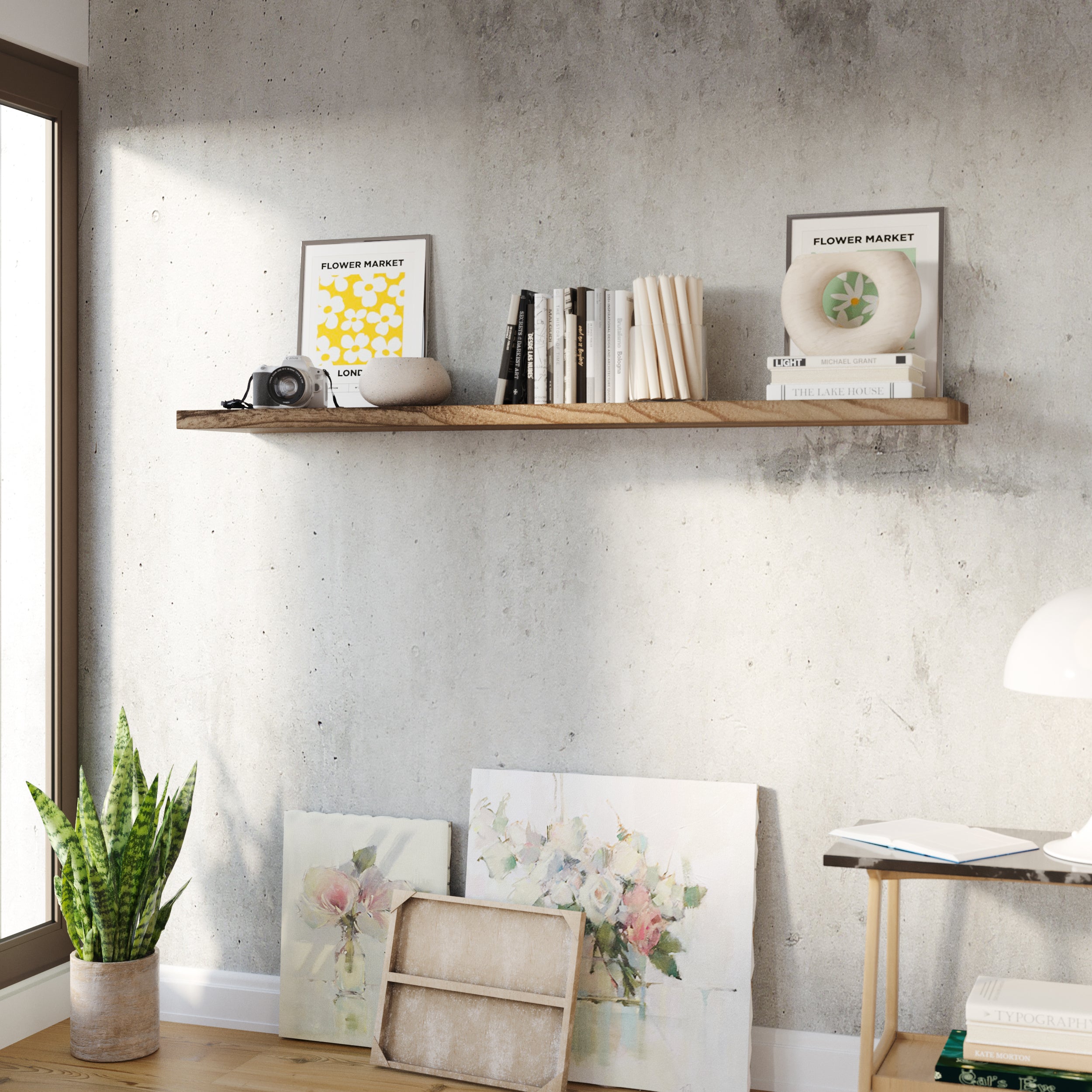 A living room setup with art frames, cactus, and a rustic hidden bracket shelf displaying a camera, candles, art frames and vintage books on a rustic wall decor