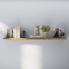 A 60 inch long floating shelf with hidden bracket mounted on a white wall, displaying vintage books, clock, flower art, and a bird design
