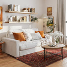 Two 60 inch long floating shelves in a special walnut finish with invisible brackets styled with books and vases over a cozy white couch. Warm tones and framed art create a welcoming living room aesthetic.