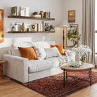 Two 60 inch long floating book shelves with invisible brackets in a dark walnut finish styled with books and vases over a cozy white couch. Warm tones and framed art create a welcoming living room aesthetic.