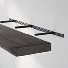 A floating shelf with a black hidden bracket system with metal rods extending from a slotted steel mount, supporting a 2'' thick rustic shelf with custom ebony  finish for a clean, floating wall shelf look.