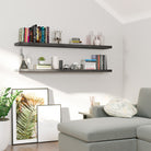 Two dark wood floating shelves with hidden brackets mounted in a cozy reading nook showcase books, cameras, small décor, and vases—balancing function and style above a soft gray sectional.