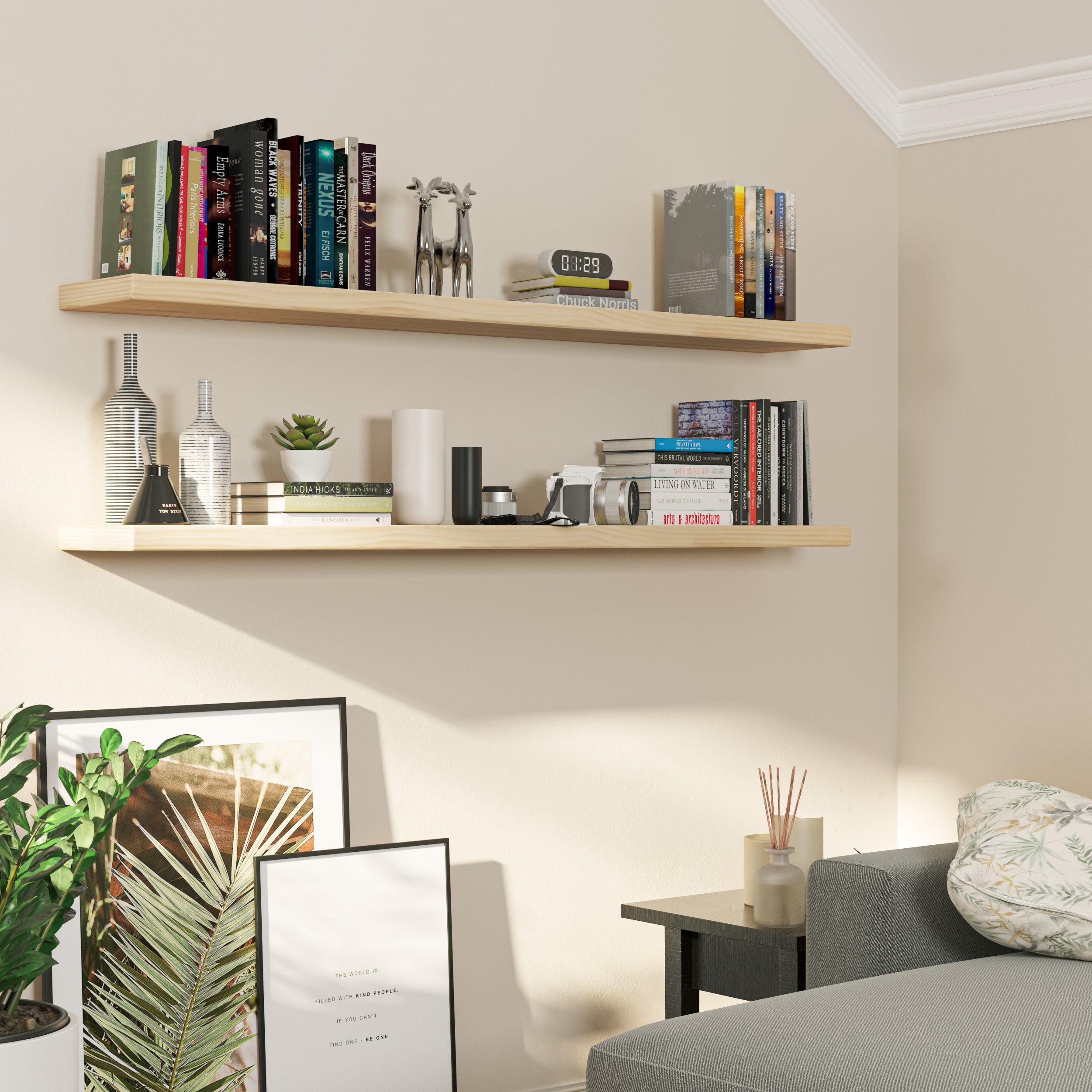 Mounted above a grey sectional, two natural-finish floating bookshelves hold books, vases, cameras, and decor, creating a warm, relaxed reading nook with natural light and earthy accents.