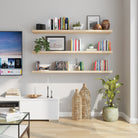 Three natural wood floating shelves neatly line a modern living room wall, holding books, plants, and decorative objects—perfect for showcasing personal style in a light-filled entertainment space.