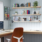 Set against blue panel walls, three natural-finish floating office shelves organize books, stationery, and decor above a tidy desk, enhancing this home office with clean lines and soft tones.