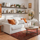 Two 72 inch long floating shelves in a dark walnut finish with invisible brackets styled with books and vases over a cozy white couch. Warm tones and framed art create a welcoming living room aesthetic.