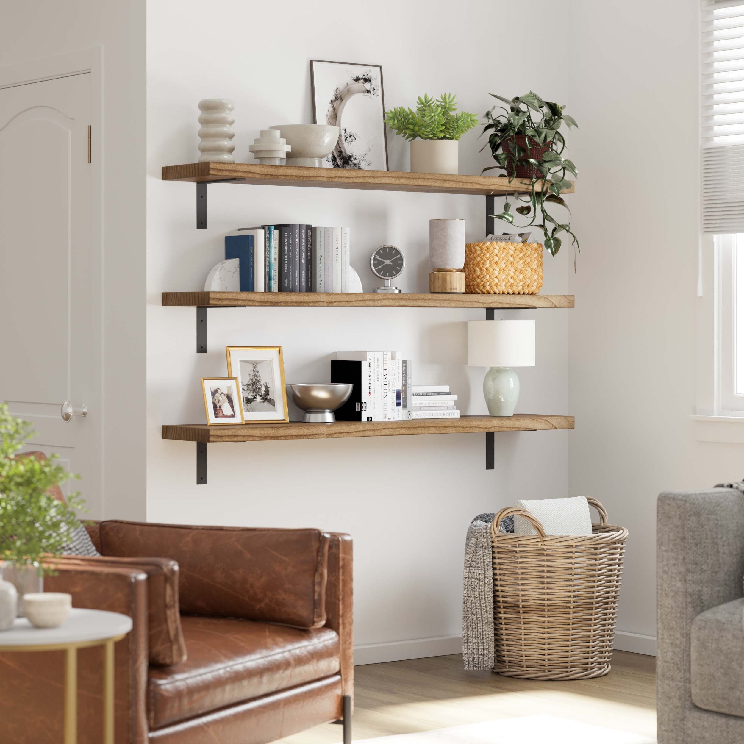 Three rustic floating shelves with plants, frames, books, and decor items create a cozy corner in a room with leather and fabric chairs.