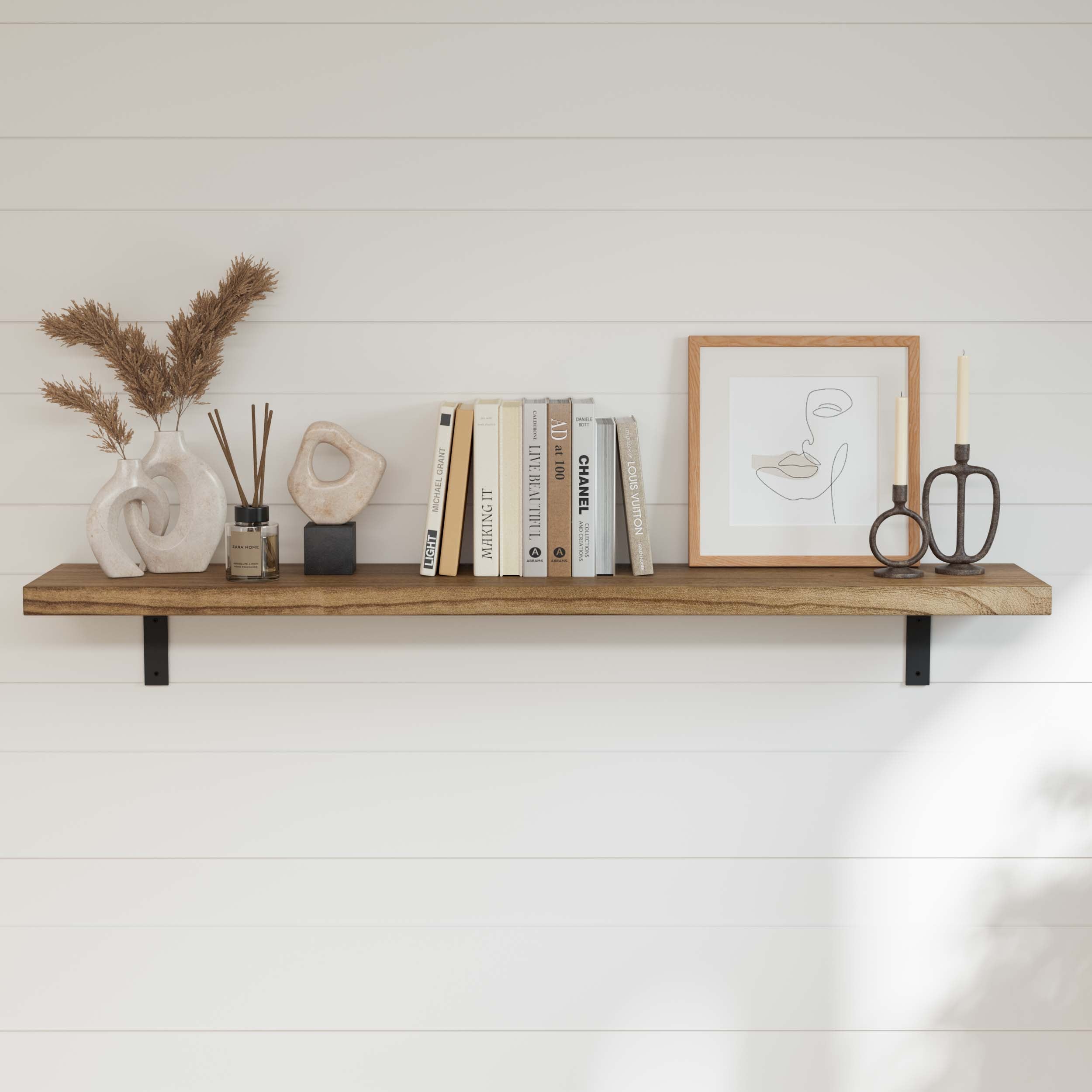 A stylish hanging shelf for wall with artistic decor, including sculptures, pampas grass, a reed diffuser, books, a framed line drawing, and candle holders.