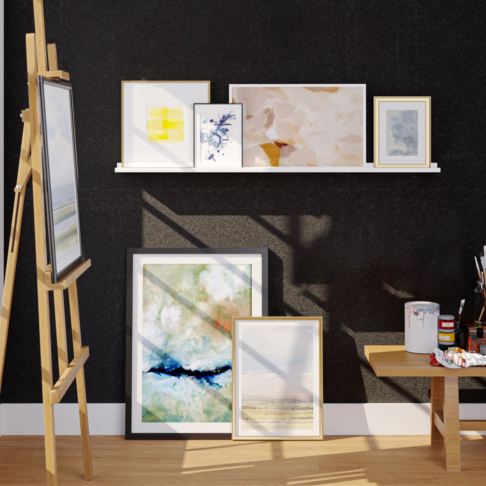 An artist’s studio with a wooden easel, paintings on shelves, and art supplies on a table against a black wall.