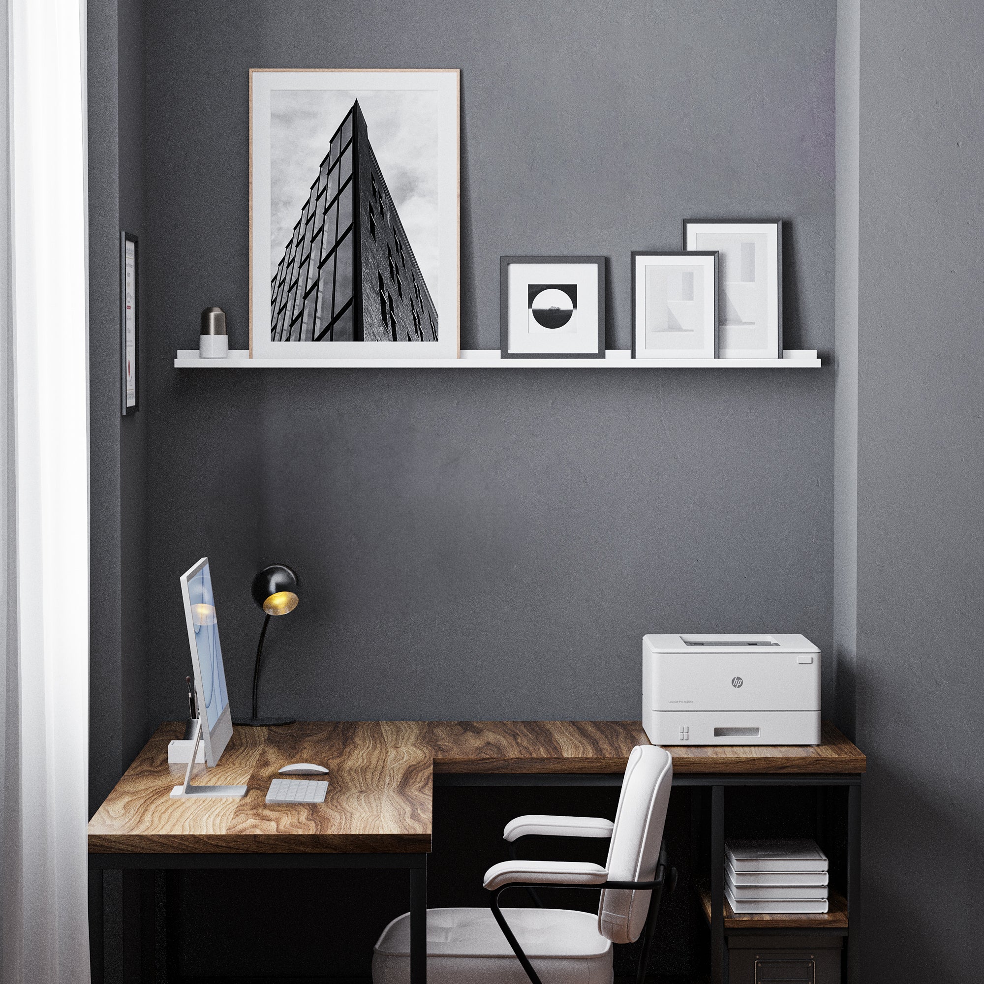 A minimalist home office with a wooden desk and chair, and a white shelf for wall displaying monochrome art above it.