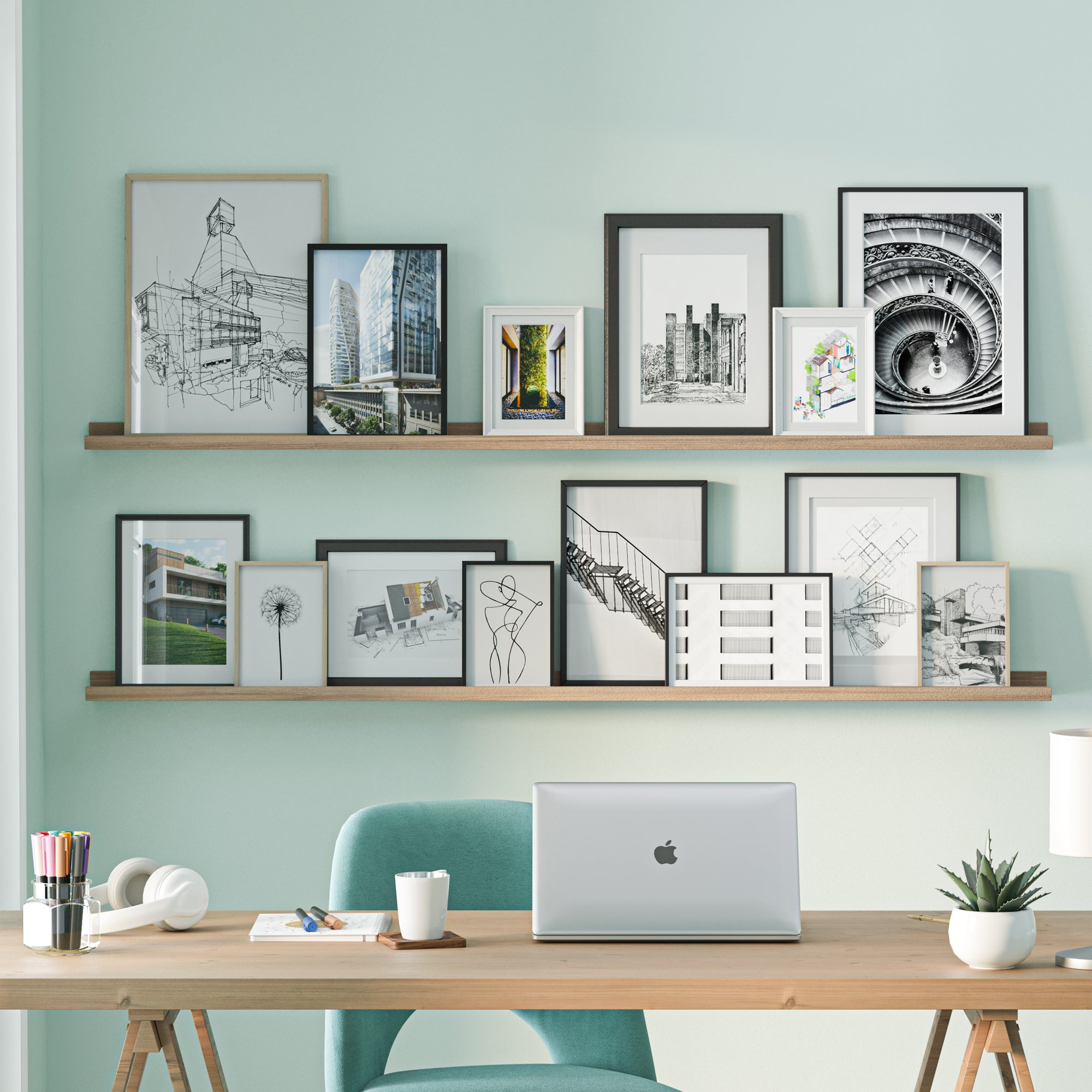 A workspace with a laptop on a wooden desk, a teal chair, and shelves for wall storage above holding various framed architectural drawings and photographs.
