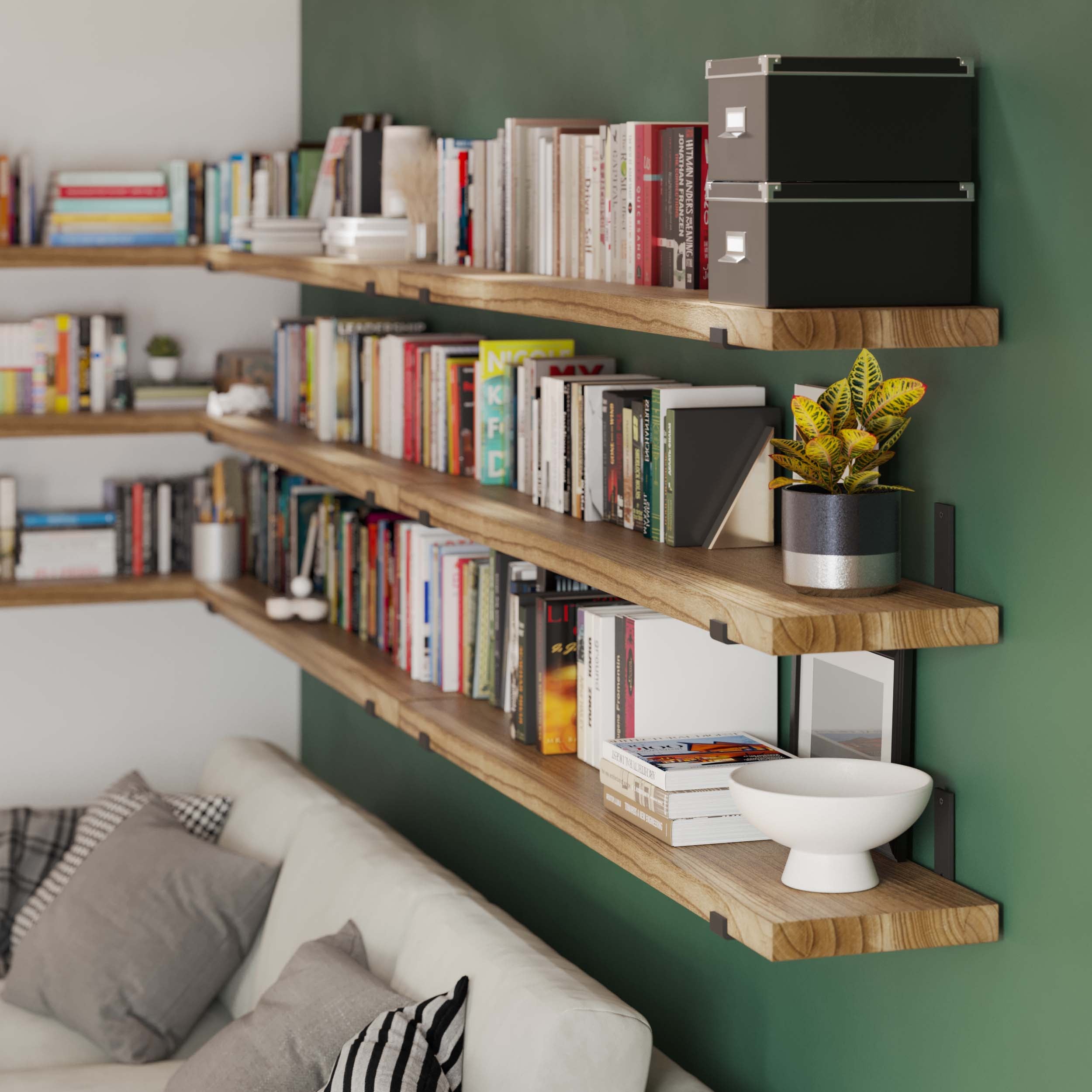 Wooden shelves filled with books and decor are mounted on a green wall behind a sofa, creating a cozy reading nook in a living room.