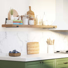 A kitchen scene with a wooden shelf holding jars, books, and cutting boards. Functional and aesthetic, enhancing the room's warmth and practicality.