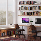 A modern office with wall bookshelves, books, computers, and warm lighting.