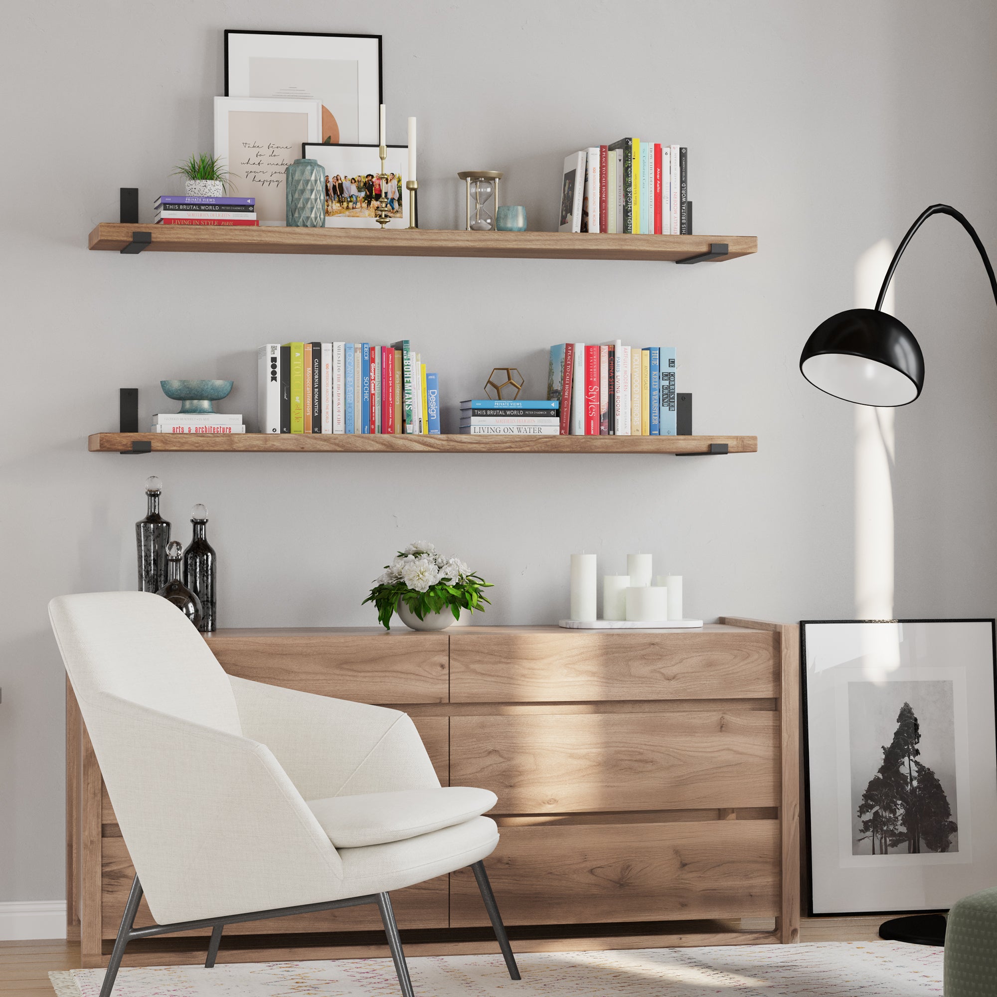Two wood floating shelves with black brackets, styled with books, candles, and decor items. Paired with a light wood dresser, white armchair, and sleek black lamp, creating a modern, cozy, and minimalist vibe.