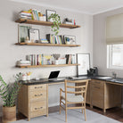 A functional home office setup featuring three long office shelves in custom provincial finish displaying books, plants, and decor. Below, a wooden desk with drawers and a black surface is paired with a wooden chair and organized stationery.