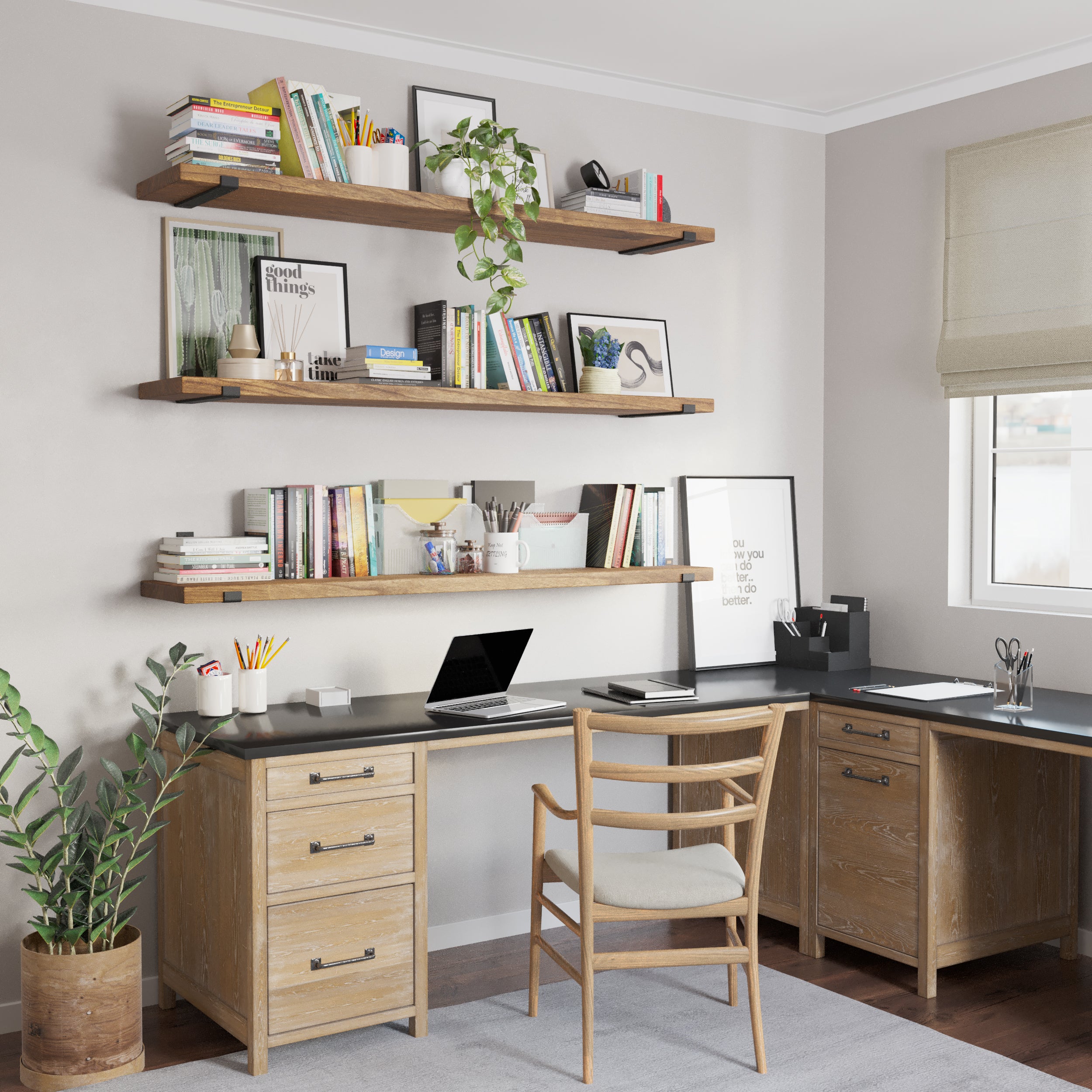 A functional home office setup featuring three long office shelves in custom provincial finish displaying books, plants, and decor. Below, a wooden desk with drawers and a black surface is paired with a wooden chair and organized stationery.