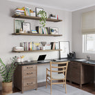 A functional home office setup featuring three wall mounted shelves in custom walnut finish adorned with books and decor. Below, an L-shaped desk with storage drawers, a wooden chair, and a potted plant create a balanced, productive environment.