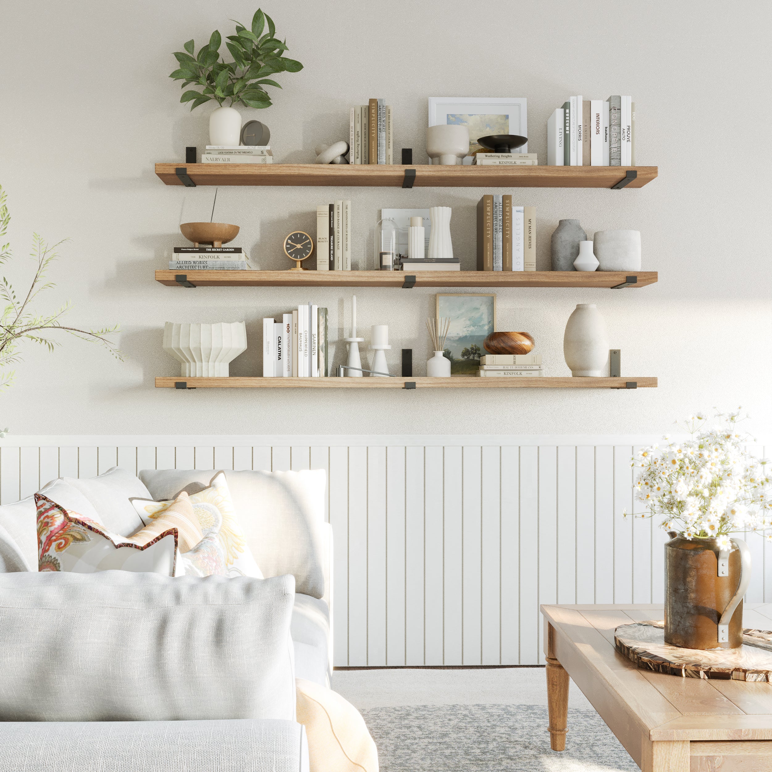 Three floating shelves in special walnut hold a mix of neutral books, vases, framed art, and candles, arranged in a cozy, layered living room setup for a serene aesthetic.