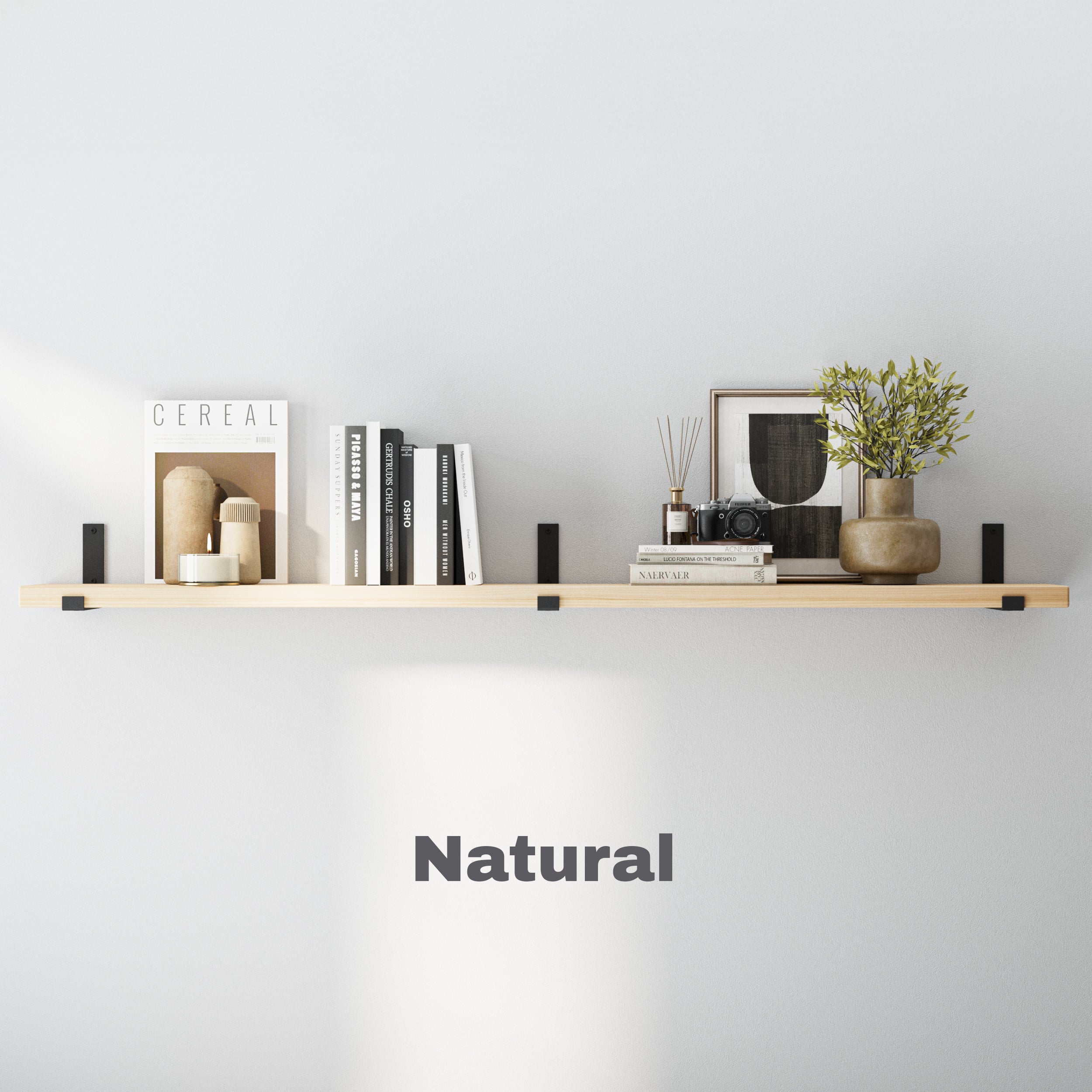 A light-toned natural finish wood floating shelf styled with books, candles, a camera, and a vase, mounted with sleek black metal brackets against a minimalist white wall.