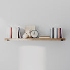 A single wall-mounted shelf in a light walnut finish, styled with neutral-toned books, vases, a framed artwork, and small home accessories. Simple yet elegant for modern interiors.