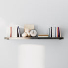 Minimalist floating shelf in sleek ebony finish styled with books, a clock, and decor. Dark wood finish and hidden black brackets create a clean, modern look against a neutral wall.