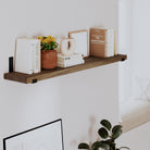 Styled wall decor shelf with books, a vase, and decor. Warm wood tone and black brackets create a modern, cozy look, perfect for living room or bedroom wall décor.