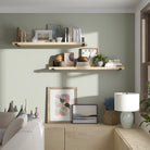 Two living room shelves styled on a sage green wall. Decorated with books, art, and plants, showcasing warm, modern living room storage and décor display.