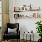 Two living room shelves above a lounge chair. Styled with books and décor, adding warmth and functional storage to a modern living room corner.
