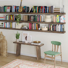 A creative bookshelf setup features multiple dark wood ledges filled with colorful books, plants, and decorative accents, transforming the wall into a stylish home library.