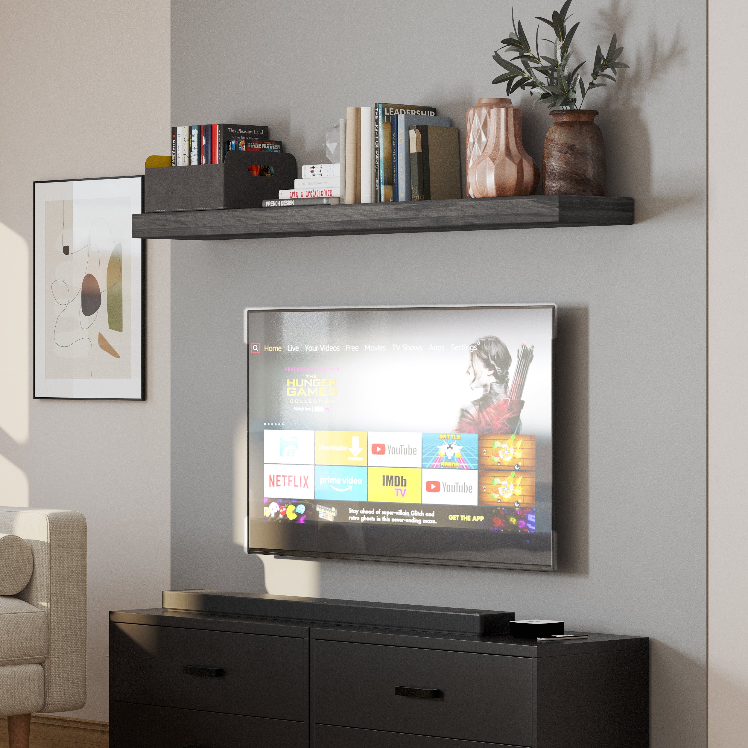 A single ebony floating shelf with invisible bracket styled above a mounted TV, holding ceramic vases, a crystal decor piece, and books. A sleek and functional addition to any media wall.
