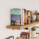 A close-up of a rustic pipe shelf filled with a variety of books and small decorative items, showcasing its robust design and the pipe bracket’s support.