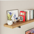 A close-up view of the rustic shelf in the office setup, highlighting the mix of books, a clock, a plant, and a decorative frame.