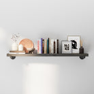 Decorative pipe shelf with books, candles, and small decorative items against a white wall.
