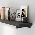 Hanging shelf for wall with industrial pipe brackets with books, a framed picture, and a vase against a gray wall.