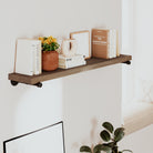 Long floating shelf with books and a plant against a white wall
