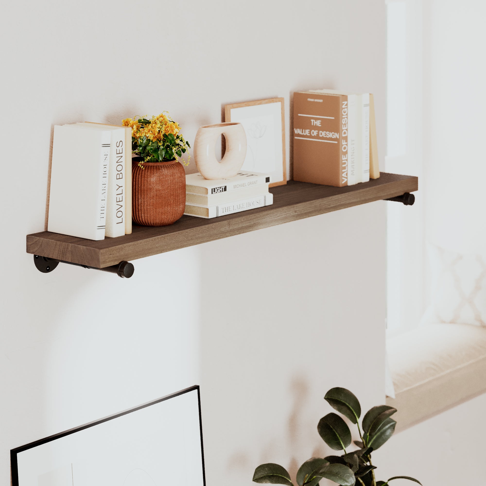 Long floating shelf with books and a plant against a white wall