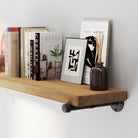 Real wood pipe bracket shelf with books, frames, and a vase against a gray wall.