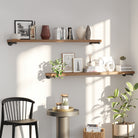 2 pieces of  60 inch long rustic shelves with black pipe brackets creating stylish vertical storage for books, framed art, and plants. Industrial floating shelves blend rustic décor, wall organization, and functional living room or bedroom storage.