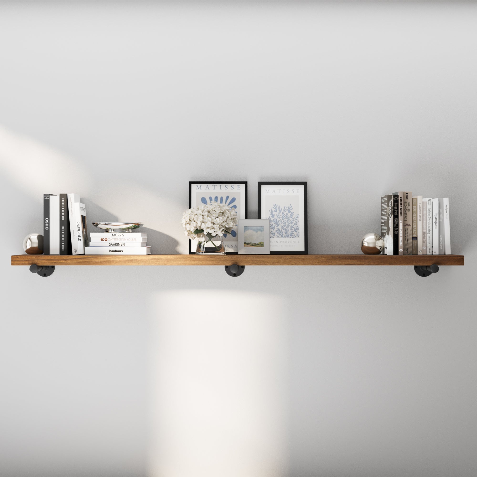 72 inch extra long industrial pipe shelf in a warm provincial finish, styled with books, framed art, and decorative accents. This extra long wall shelf blends rustic farmhouse charm with industrial décor for living rooms, offices, or bedrooms